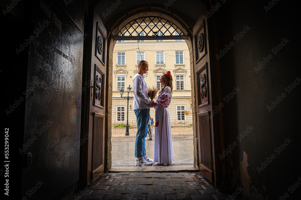 Profile view of a young couple in love in Ukrainian national dress in an embroidered shirt embracing while standing in a doorway. View from the corridor through the doorway. Creating a family