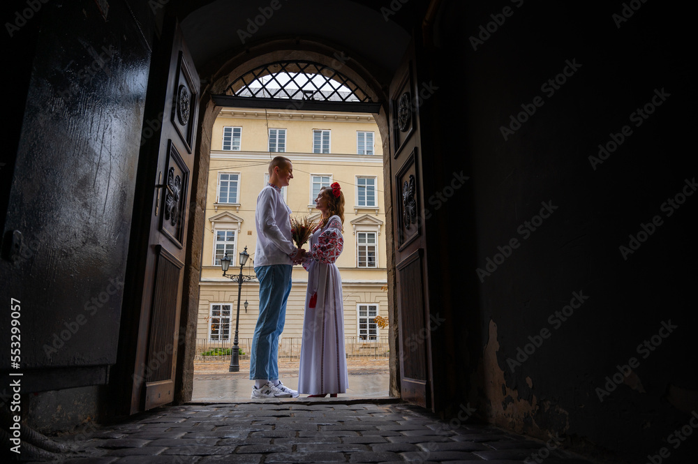 Profile view of a young couple in love in Ukrainian national dress in an embroidered shirt embracing while standing in a doorway. View from the corridor through the doorway. Creating a family