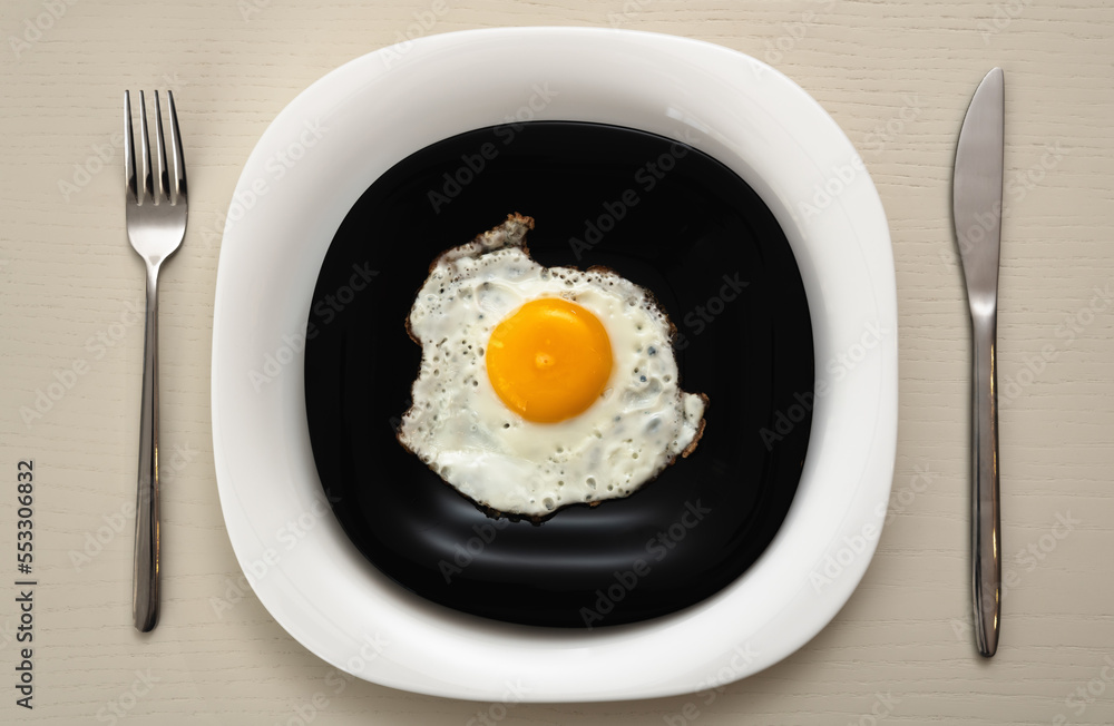 Fried eggs on a black and white plate with serving at a white table Fried eggs on a black and white plate with serving at a white table