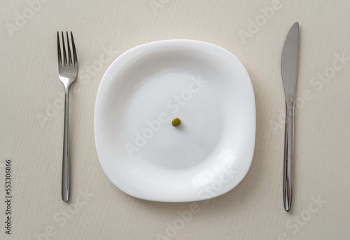 A small pea on a white plate on a white table with a knife and fork, minimum calories