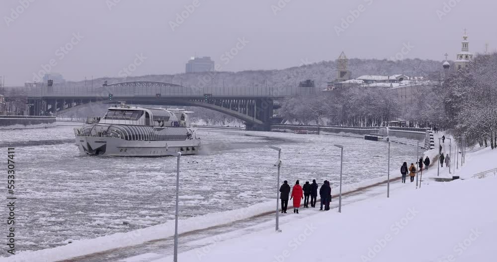 A pleasure boat sails on a frozen river breaking ice after a snowfall in the city A pleasure boat sails on a frozen river breaking ice after a snowfall in the city