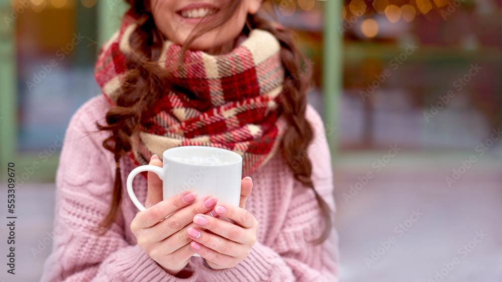 girl walking with coffee on street of winter holidays city. smiling woman in checkered red scarf drink hot coffee with marshmallow in white mug. girl walking with coffee on street of winter holidays city. smiling woman in checkered red scarf drink hot coffee with marshmallow in white mug.