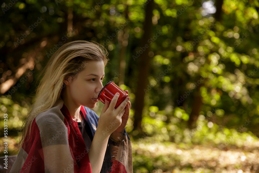 young caucasian woman drinking from red metal mug in nature.background blurred. selective focus. High quality photo young caucasian woman drinking from red metal mug in nature.background blurred. selective focus. High quality photo