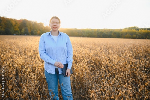 Young farmer woman standing in soy field in summer time, holding tablet and monitoring crop growth © Serhii