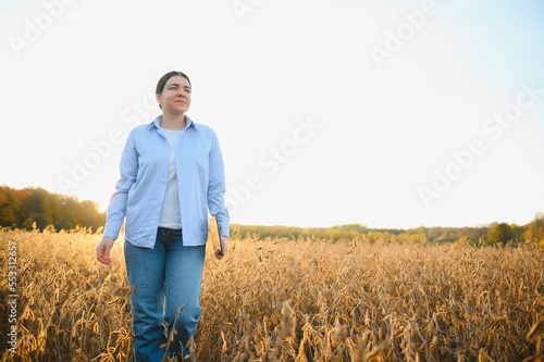 Portrait of young female farmer standing in soybean field examining crop. © Serhii
