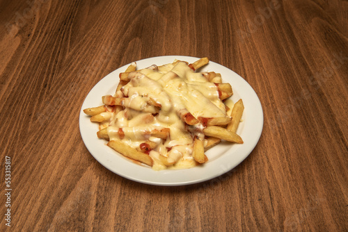 a portion of French fries with lots of melted cheese with fried bacon and ketchup