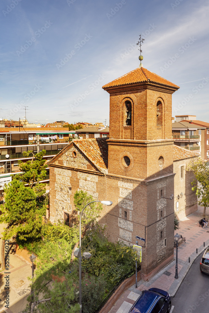 A neighborhood church in Madrid, Spain, with a mud brick bell tower between the buildings and surrounded by trees