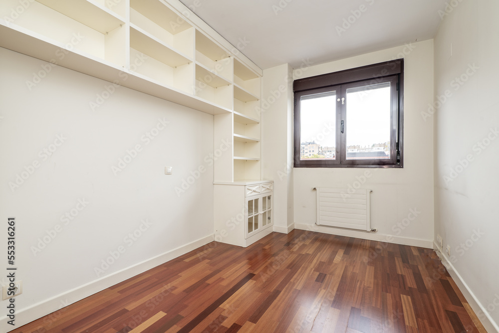 An empty room with a white lacquered wooden tall bookcase with a low cabinet and a reddish parquet floor An empty room with a white lacquered wooden tall bookcase with a low cabinet and a reddish parquet floor