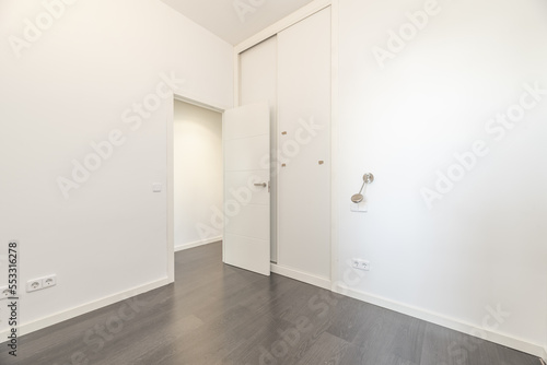 An empty room with smooth white walls, a floor-to-ceiling built-in wardrobe with sliding doors and gray wooden floors