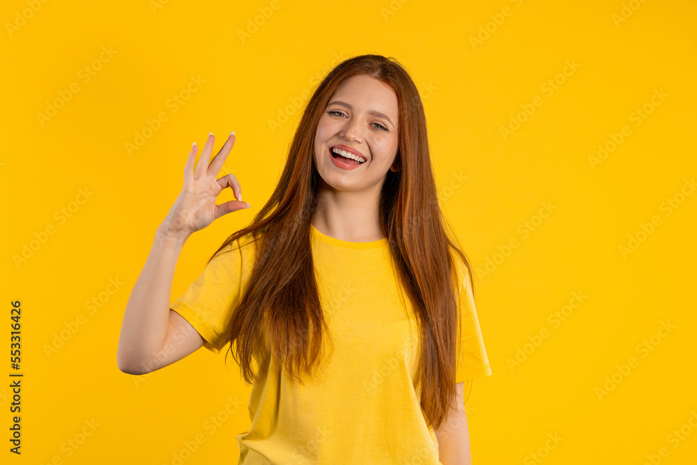Pretty woman makes hand sign okay, ok gesture. Happy ginger girl, correct perfect choice, great deal, yellow background. Positive female model smiles to camera, approval, trust concept Pretty woman makes hand sign okay, ok gesture. Happy ginger girl, correct perfect choice, great deal, yellow background. Positive female model smiles to camera, approval, trust concept