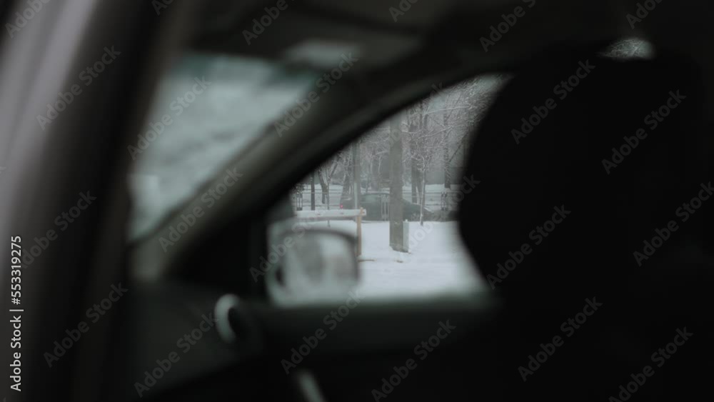 View from inside of car standing on parking lot with barrier and city road on winter day. Unrecognizable man exits car and closes door. Car is driving on snowy road. View from inside of car standing on parking lot with barrier and city road on winter day. Unrecognizable man exits car and closes door. Car is driving on snowy road.