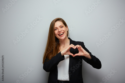 Smiling business woman in black suit holding heart figure with fingers, isolated portrait.