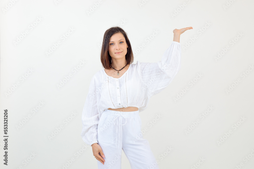 Portrait of young happy woman wearing white blouse, trousers, standing, raising hand with open palm, looking at camera. Portrait of young happy woman wearing white blouse, trousers, standing, raising hand with open palm, looking at camera.