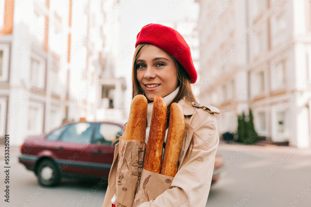 close up outdoor portrait of smiling happy girl in french outfit posing at camera with happy smile, holding fresh bread. Walking, weekend, recreation