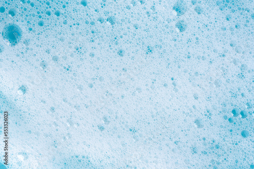 Texture of white foam on blue background. Foam cosmetic product for skincare procedure. White foam texture macro background. Cosmetic product foamy smudges with bubbles. Foamy skin care product