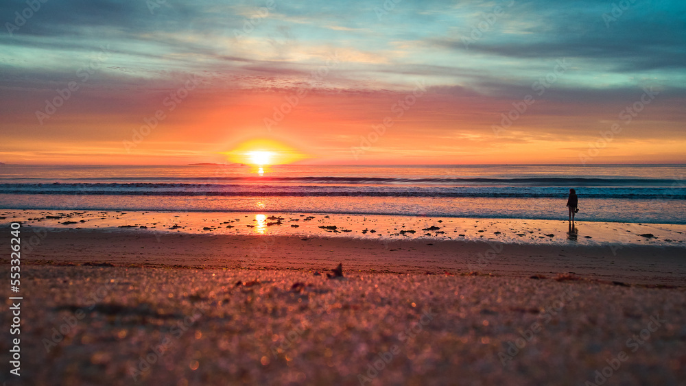 Tourist walking on sandy beach during stunning sunrise light with ocean waves Tourist walking on sandy beach during stunning sunrise light with ocean waves