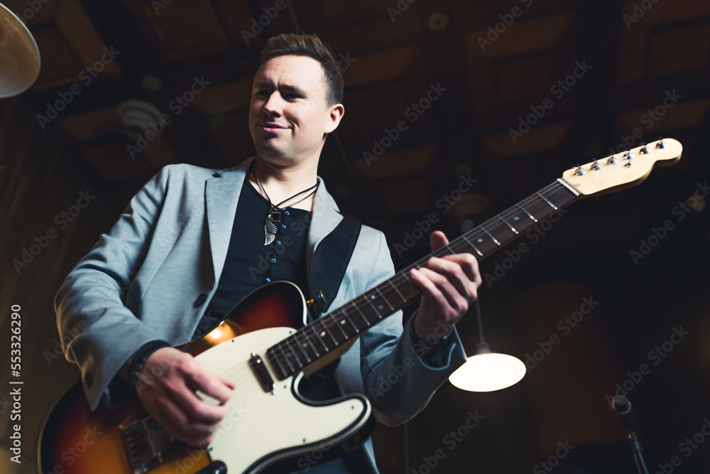 Obraz premium Musician playing on a guitar. Caucasian mid adult man in a rock band playing his guitar. Stage lightening. Low angle indoor shot. High quality photo