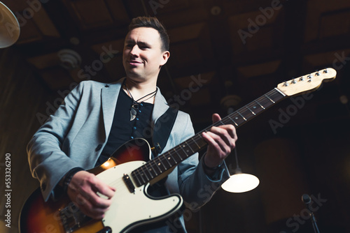 Musician playing on a guitar. Caucasian mid adult man in a rock band playing his guitar. Stage lightening. Low angle indoor shot. High quality photo