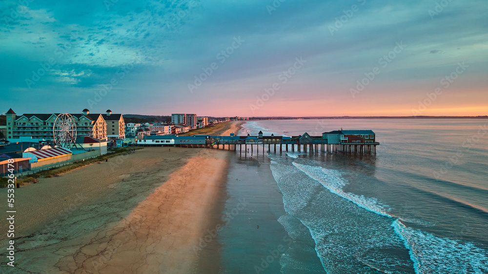 Fototapeta premium Aerial view over beach in Maine during sunrise with town and old wood pier of shops