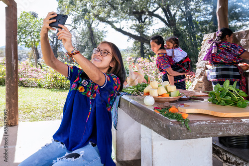 Chica haciendose una selfie con el telefono celular a ella su abuela y su mama. Familia cocinando al aire libre.  photo