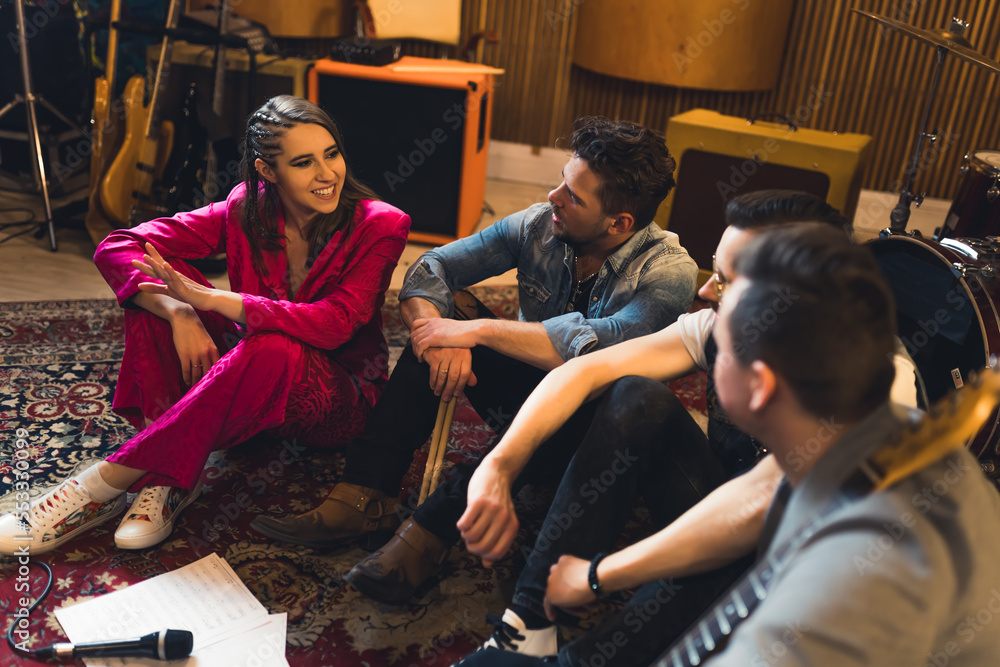 Excited band members sitting together on a carpet. Female vocalist talking to her band partners about a new song idea. High quality photo