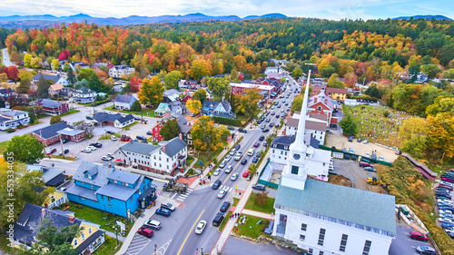 Stunning aerial over small Vermont town of Stowe surrounded by fall foliage and focus on white church photo