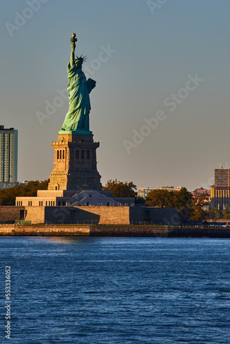 Light filling in half of Statue of Liberty in New York City from waters with golden hues