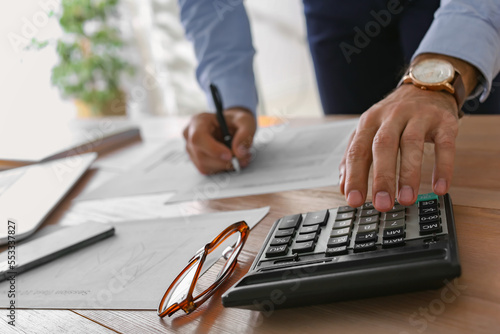 Tax accountant with calculator working at table in office, closeup