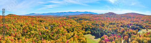 Panoramic aerial over peak fall forest mountains in Vermont with blue skies