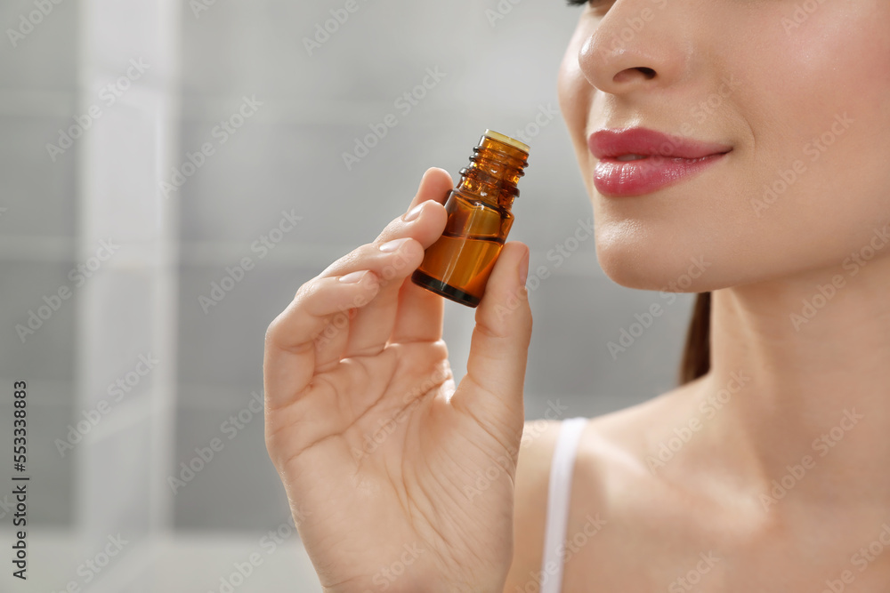 Fototapeta premium Young woman smelling essential oil indoors, closeup