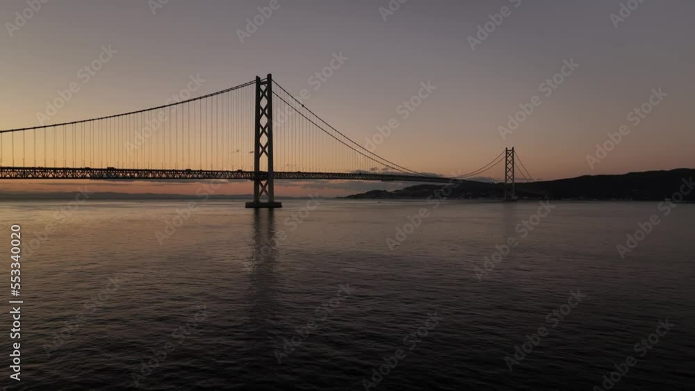 Flying low over water towards long suspension bridge at dawn Flying low over water towards long suspension bridge at dawn