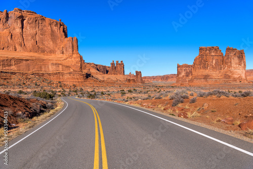 Desert Road - A sunny Winter morning view of a desert road winding towards towering red sandstone formations in Arches National Park, Utah, USA. 