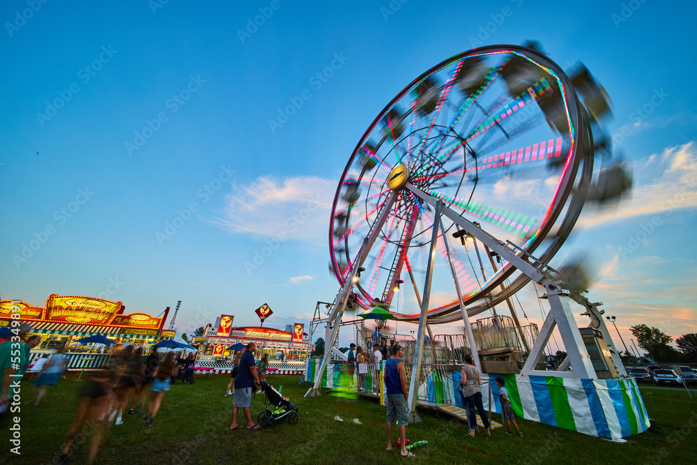 Carnival county fair with ferris wheel attraction at dusk