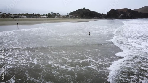 Surfer leaving beach heading into waves for next surf session. Aerial tracking shot. 