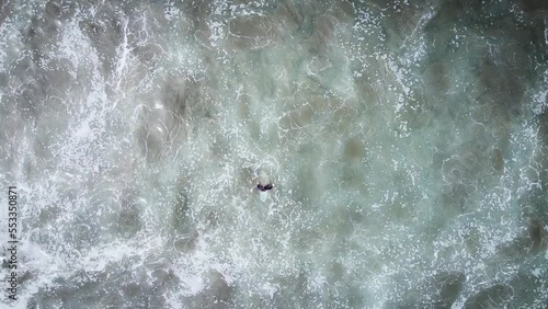Aerial top down view of surfer treading water as big waves approach. 