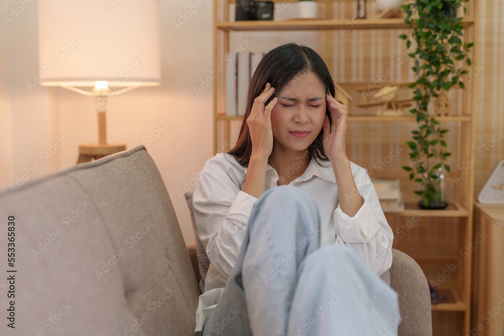 Young Asian woman suffering from illness, stress, depression from work sitting alone on sofa at home frustrated. Desperate Asian woman feeling alone. Young Asian woman suffering from illness, stress, depression from work sitting alone on sofa at home frustrated. Desperate Asian woman feeling alone.