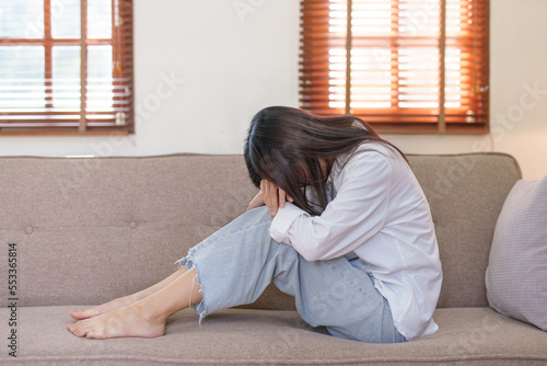 Young Asian woman suffering from illness, stress, depression from work sitting alone on sofa at home frustrated. Desperate Asian woman feeling alone.