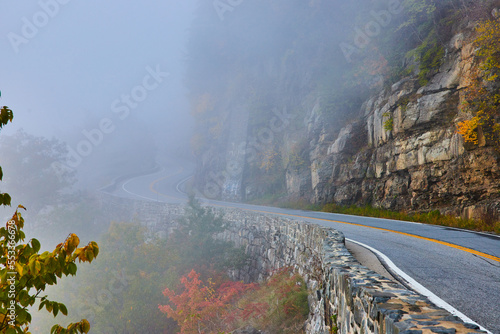 Stone wall along stunning road against cliffs winding away into fog