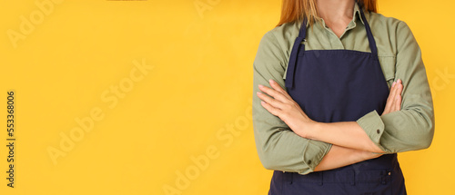 Young woman wearing apron on yellow background with space for text © Pixel-Shot