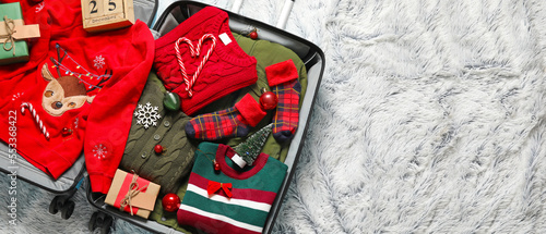 Open suitcase with packed clothes on plaid, top view. Christmas holidays concept