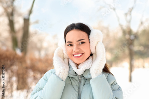 Beautiful smiling woman in warm clothes and earmuffs on cold winter day