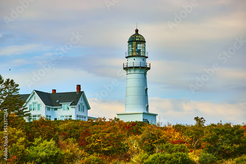 Large lighthouse by home in colorful fall forest with overcast sky