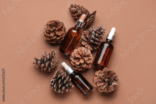 Bottles with essential oil and pine cones on brown background