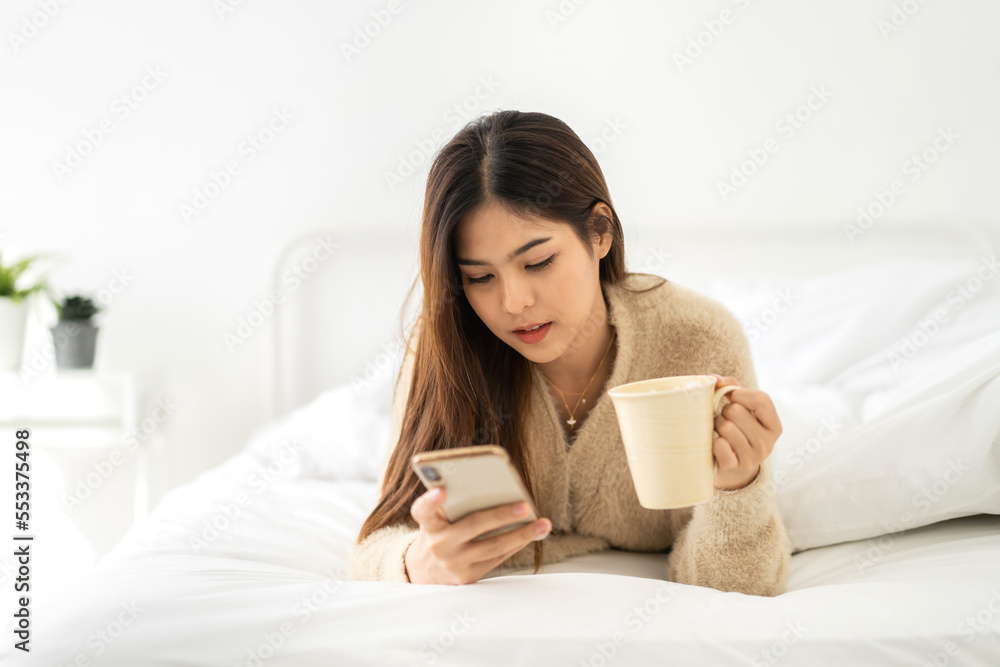 Portrait of smiling happy beautiful asian woman relaxing using digital smartphone.Young asian girl looking at screen typing message and playing game online or social media at home Portrait of smiling happy beautiful asian woman relaxing using digital smartphone.Young asian girl looking at screen typing message and playing game online or social media at home