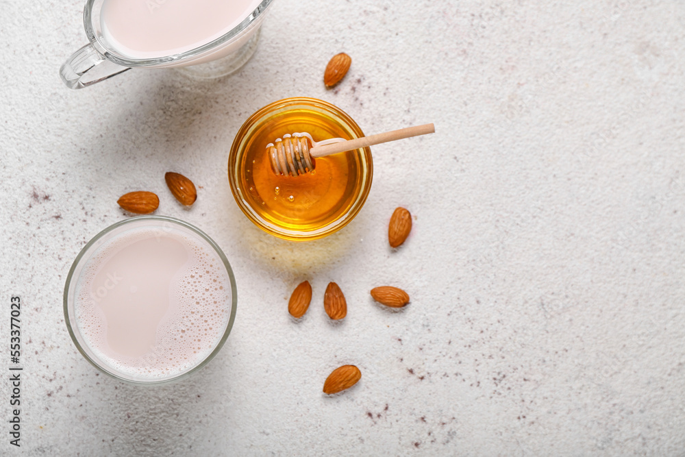 Glass of healthy almond milk, bowl with honey and nuts on light background Glass of healthy almond milk, bowl with honey and nuts on light background