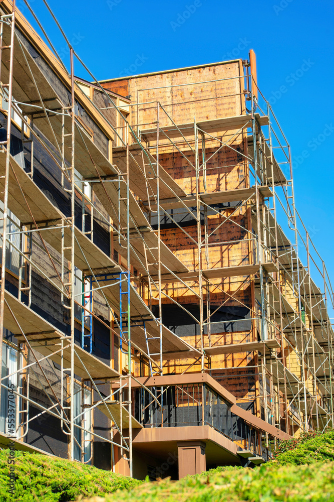 Construction on modern building with wooden walls and metal scafolding on exterior of the building in the downtown city with trees