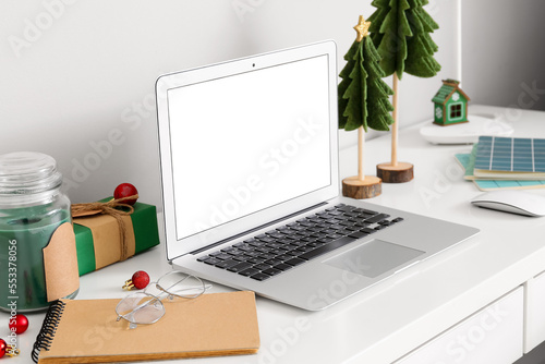 Workplace with laptop, Christmas trees, gift and candle near light wall in office