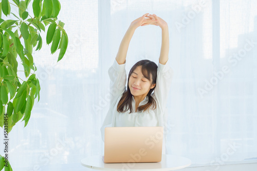 パソコン作業に疲れて伸びをする若い女性