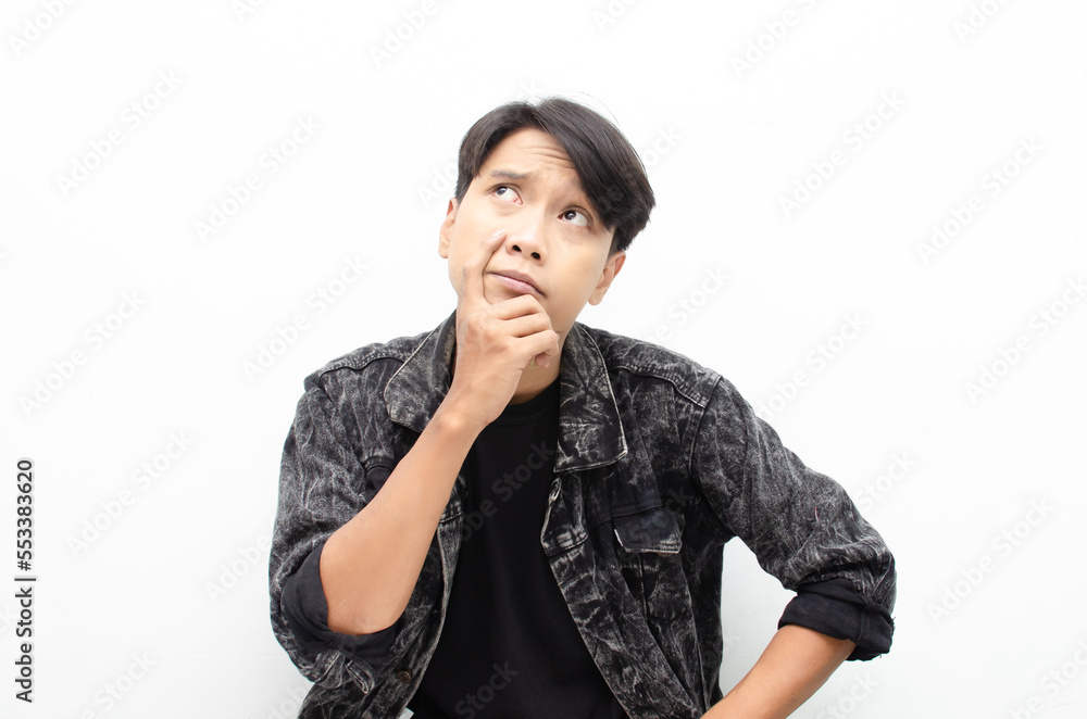 Thoughtful asian man wearing jeans jacket thinking and wondering with hand touching skin as thinking gesture isolated over whitr background Thoughtful asian man wearing jeans jacket thinking and wondering with hand touching skin as thinking gesture isolated over whitr background