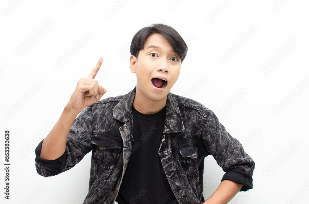 A young Asian man is looking surprised while pointing his finger upward. great idea concept. aha I have an idea expression. A young Asian man is looking surprised while pointing his finger upward. great idea concept. aha I have an idea expression.